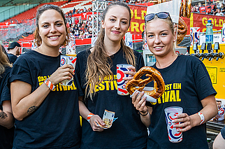 Drei Mitarbeiterinnen die mit Veranstaltungsshirt, Plastikbechern und Brezen bei einem Event im Ernst Happel Stadion stehen